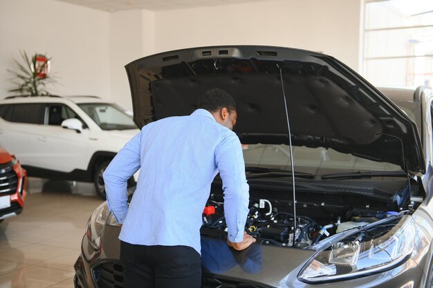 Foto um belo homem africano a escolher um carro novo na concessionária.