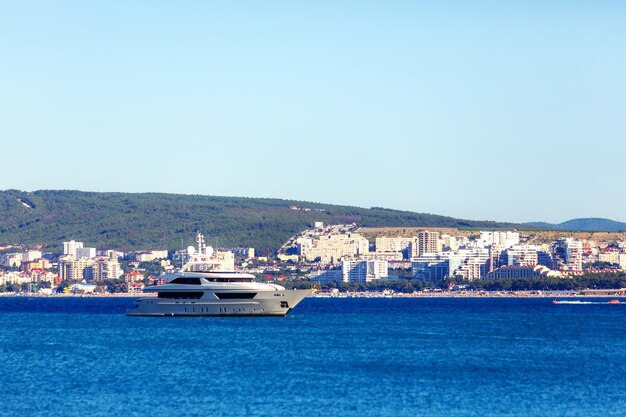 Um belo iate branco de dois decks está localizado na Baía de Gelendzhik, tendo como pano de fundo a cidade de Gel