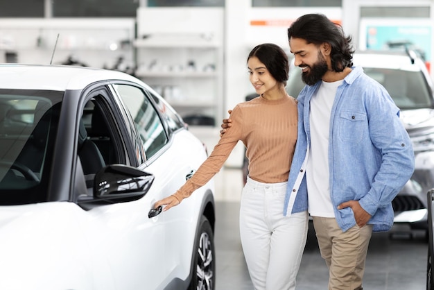 Foto um belo jovem casal indiano a escolher um carro de família na sala de exposições.