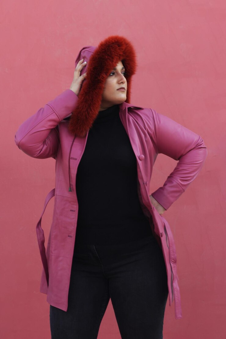 Foto um belo modelo posando em jaqueta longa de couro rosa com um elegante chapéu de pele vermelha