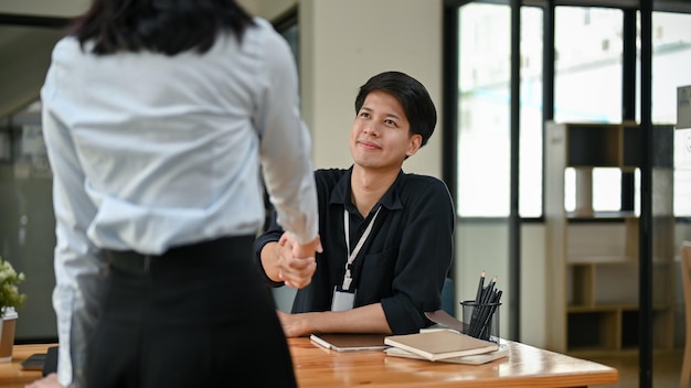 Um belo trabalhador de escritório asiático apertando a mão de uma nova colega no escritório