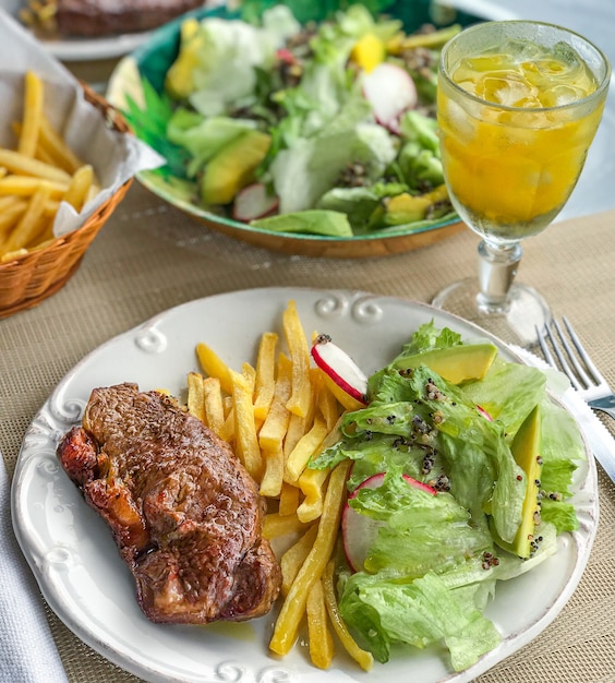 Um bife acompanhado de uma salada verde vegana com abacate, rabanete, alface e quinua.