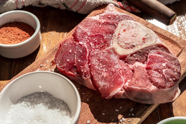 Um bife de ossobuco de carne crua fresca em uma placa com guarnições em uma mesa de madeira Conceito de proteína animal Comida italiana Vista aérea