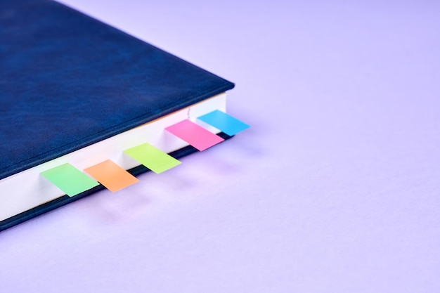 Um bloco de notas de escritório com marcadores de página pegajosos coloridos entre as páginas no fundo roxo