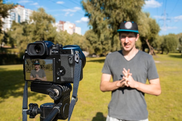 Um blogueiro masculino faz uma gravação de vídeo em uma câmera do lado de fora em um estilo de vida ensolarado