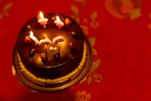 Um bolo de aniversário de chocolate com velas acesas fica na mesa vermelha