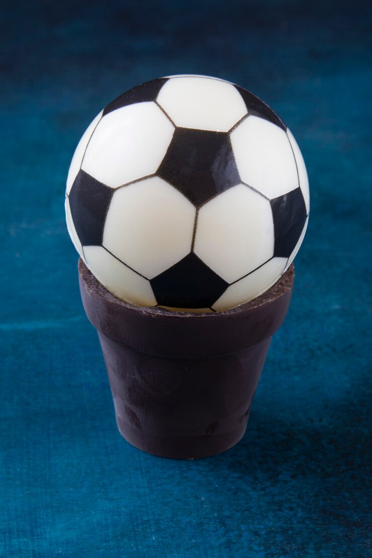 Foto um bolo em forma de bola preta e branca em um pote de chocolate sobre a mesa como um presente para um fã de futebol europeu