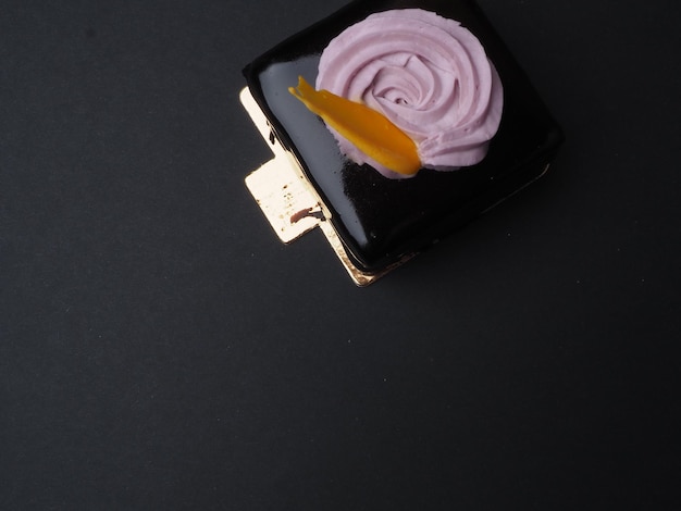 Um bolo quadrado preto com uma cobertura roxa e um redemoinho de creme.