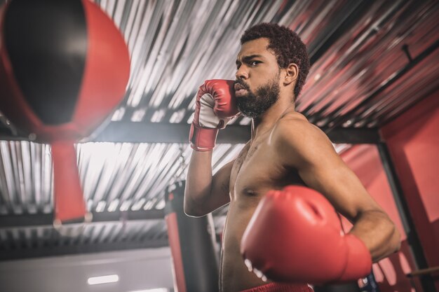 Um bom chute. kickboxer afro-americano se exercitando em uma academia e chutando o saco de areia