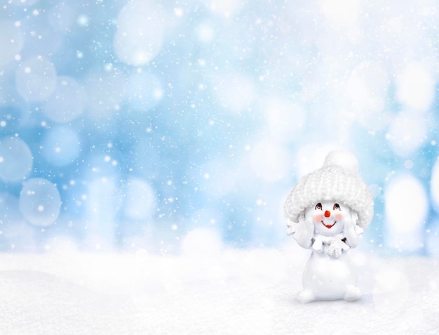 um boneco de neve com um chapéu fica na neve em um fundo azul com bokeh