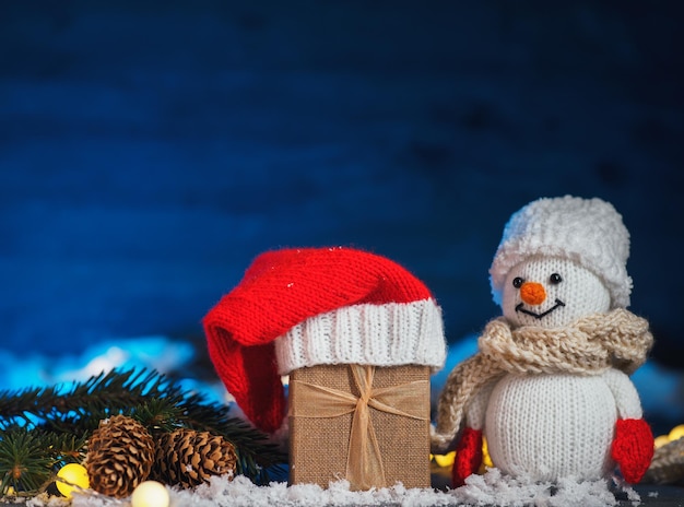 Um boneco de neve e uma caixa de presente de Natal em um espaço de cópia de neve falsa de fundo azul