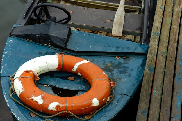 Um bote salva-vidas atracado perto de um cais de madeira No interior há um remo de madeira e um colete salva-vidas Uma velha lancha com volante Más condições de trabalho Uso de equipamentos antigos