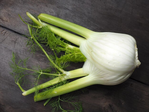 Um bulbo de funcho verde e branco está sobre uma mesa de madeira.