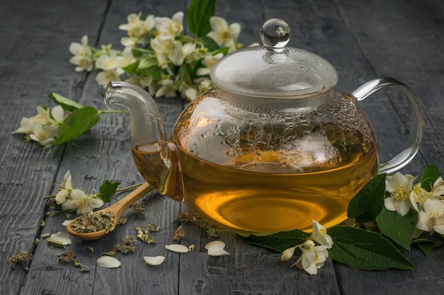 Um bule de chá de jasmim de vidro sobre uma mesa de madeira preta. Uma bebida revigorante que faz bem à saúde.