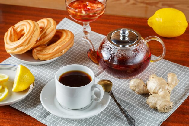 Um bule de chá e uma xícara de chá forte e aromático na mesa em um guardanapo ao lado de gengibre e geleia de limão e donuts.