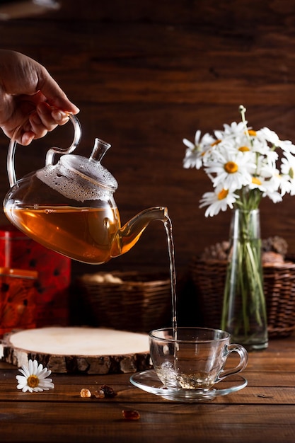 Um bule e uma caneca de chá em uma mesa de madeira e um buquê de margaridas