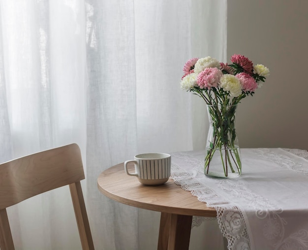 Um buquê de ásteres em um vaso de vidro, uma xícara de café em uma mesa redonda na sala de estar