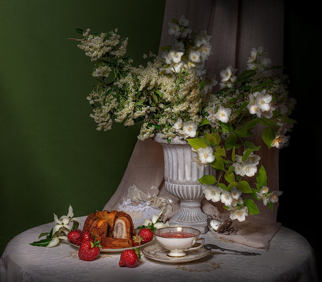 um buquê de flores em um vaso com uma sobremesa com morangos em um fundo verde