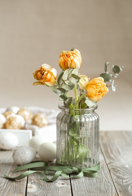 Um buquê de flores em um vaso de vidro com elementos decorativos em uma parede borrada. Conceito de férias da Páscoa.