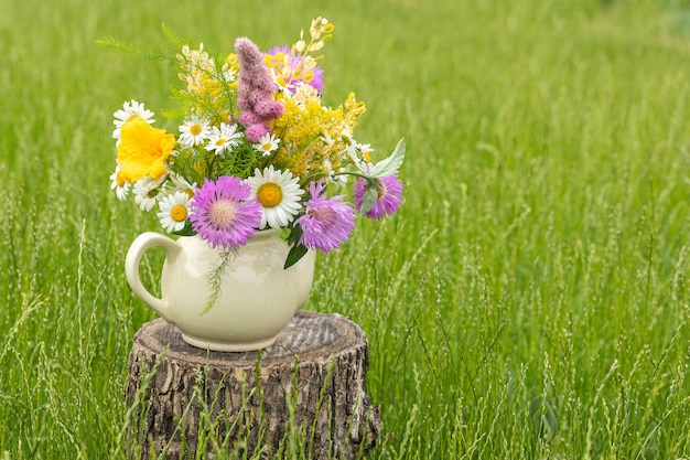 Um buquê de flores silvestres em um velho bule de vila pequena em um fundo de relva verde. Copie o espaço.