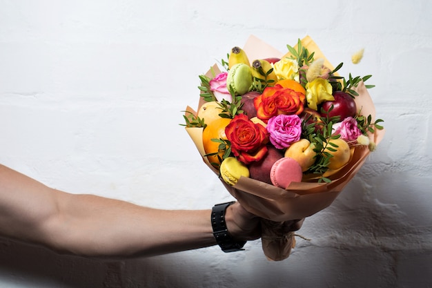 Um buquê de frutas e flores é dado por um homem em um fundo branco