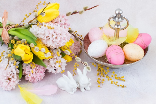 um buquê de jacintos e tulipas, duas figuras de coelhos e ovos de Páscoa em um vaso