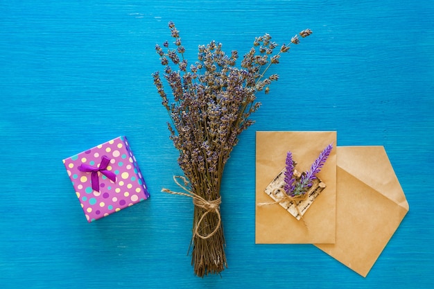 Um buquê de lavanda seca e envelopes repousam sobre uma placa de madeira azul