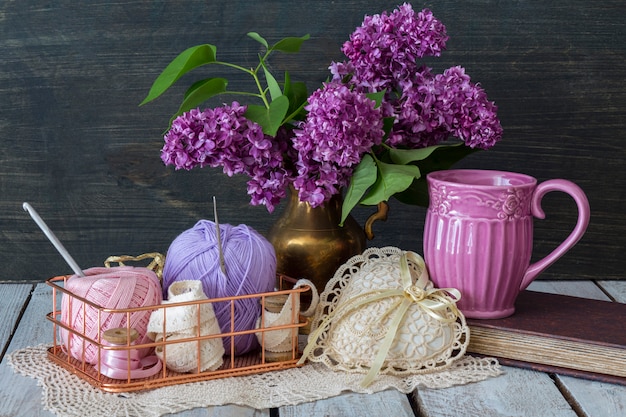 um buquê de lilases roxos está em um vaso na mesa, um livro, em uma cesta de fio
