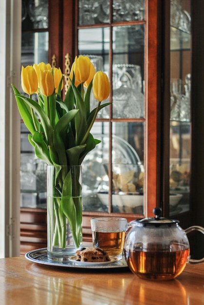 Foto um buquê de lindas tulipas amarelas em um vaso na mesa de jantar com um bule de chá uma xícara de chá