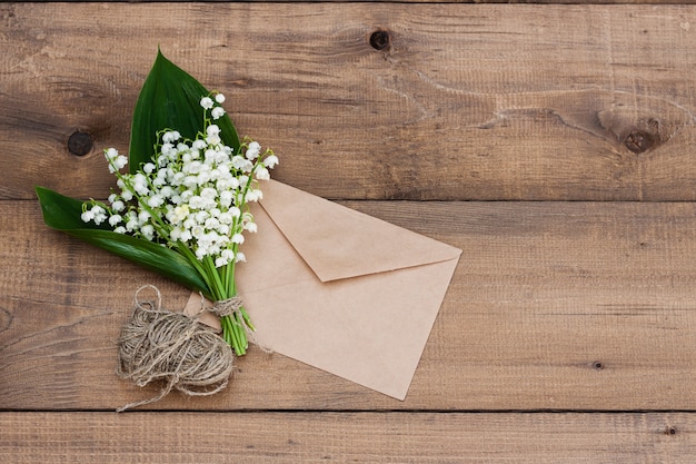 Um buquê de lírios do vale e um envelope em uma superfície de madeira