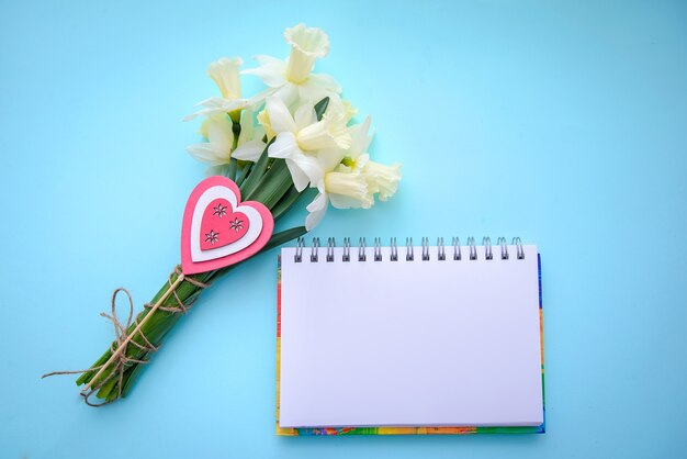 Um buquê de narcisos com um coração e um caderno em um azul