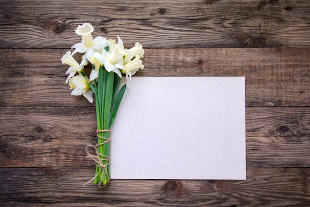 Um buquê de narcisos e um pedaço de papel com fundo de madeira