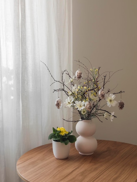 Um buquê de Páscoa em um vaso de cerâmica e uma flor de prímula em uma panela em uma mesa redonda de madeira na sala de estar Decoração da Casa da Páscoa