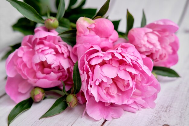 Um buquê de peônias rosa carmesim deitado em uma mesa de madeira