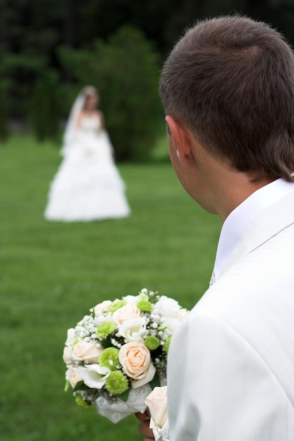 Um buquê de rosas brancas nas mãos do noivo olhando para a noiva