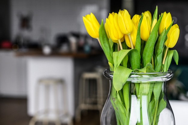 Um buquê de tulipas amarelas em um vaso de vidro no fundo do interior do apartamento. Vista lateral