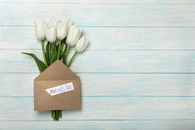 Um buquê de tulipas brancas com nota de amor e envelope em tábuas de madeira azuis. dia das mães