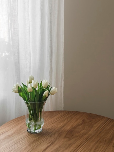Um buquê de tulipas brancas em um vaso de vidro em uma mesa de madeira na sala de estar