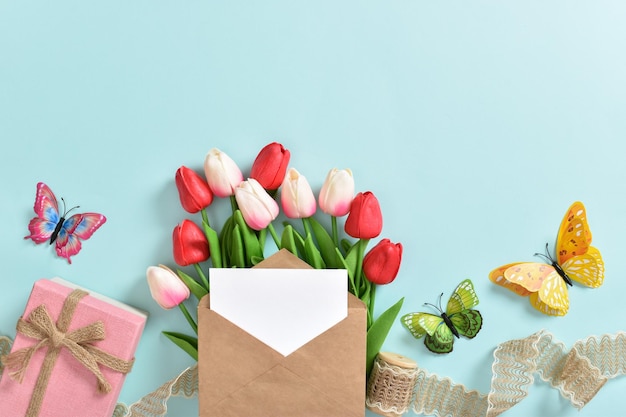 Um buquê de tulipas com um cartão postal e um presente em um fundo azul claro