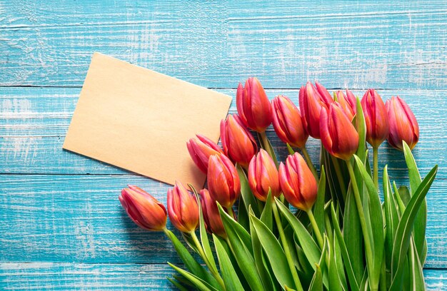 Um buquê de tulipas e um pedaço de papel para texto em um fundo de madeira