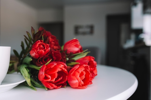 Um buquê de tulipas vermelhas na mesa e uma xícara de café branca. Conceito de um cartão de felicitações.