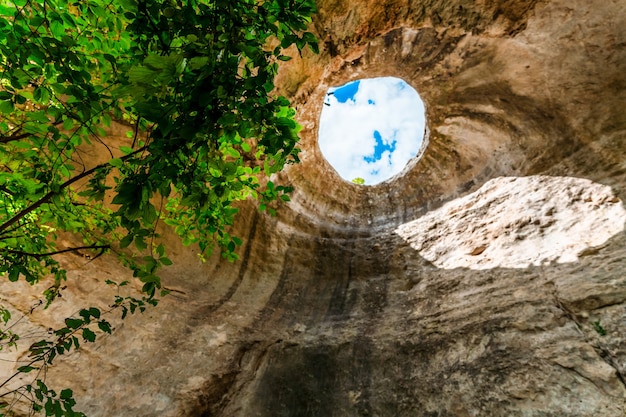 Um buraco de onde os raios de sol e o céu são visíveis fora de uma caverna subterrânea