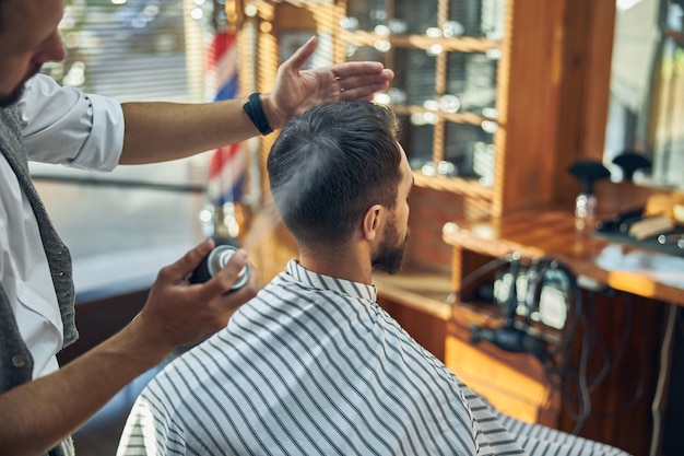 um cabeleireiro criativo borrifando o cabelo de seu cliente enquanto trabalhava em uma barbearia