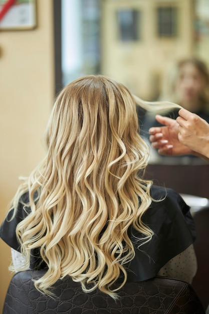 Um cabeleireiro em um salão de beleza fazendo penteados para um cliente com um ferro de cabelo