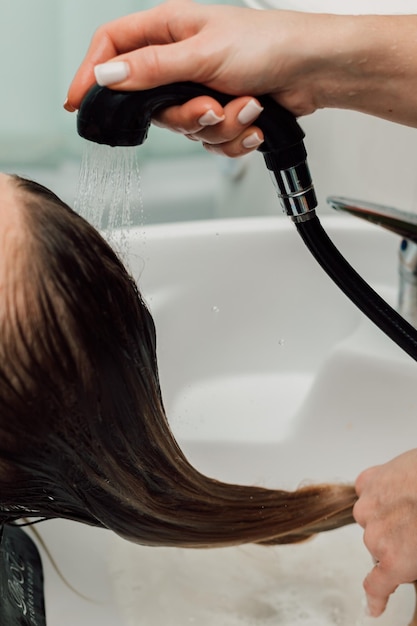 Um cabeleireiro lava o cabelo de uma loira em um salão de beleza Cuidados e tratamento capilares