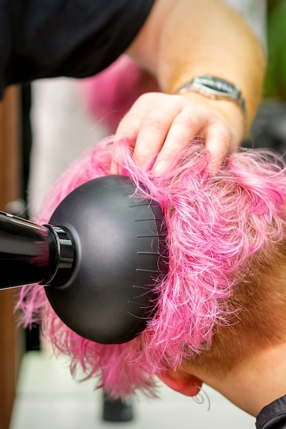 um cabeleireiro profissional secando o cabelo rosa estiloso de uma cliente com um secador de cabelo