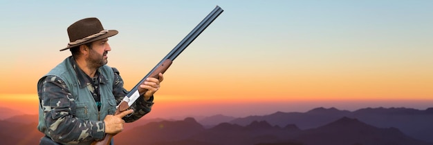 Um caçador camuflado e uma arma nas mãos no início da manhã no topo de uma montanha está procurando um alvo linda paisagem montanhosa a abertura da caça