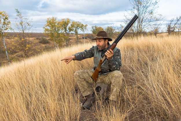 Um caçador com uma arma nas mãos e com roupas de caça na floresta de outono em busca de um troféu
