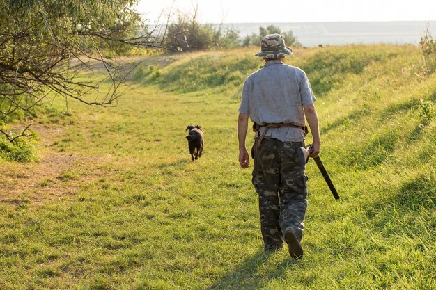 Um caçador com uma arma nas mãos em roupas de caça na floresta de outono em busca de um troféu