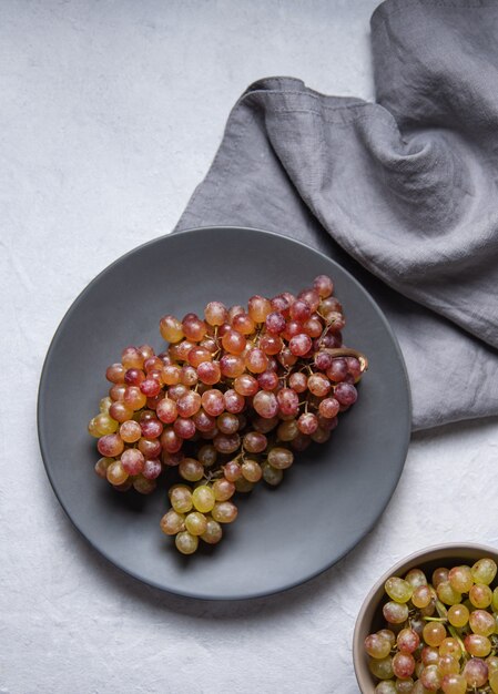 Um cacho de uvas verdes suculentas em um prato cinza com guardanapo sobre uma mesa de luz. Vista do topo